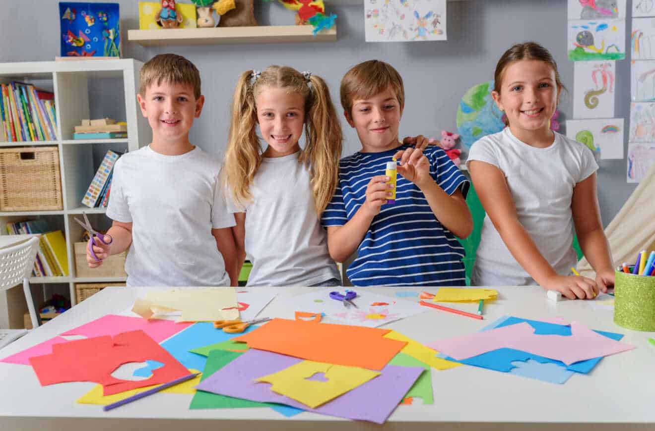 Four kids smiling and holding paper cutouts, posing for the camera with joy and excitement.