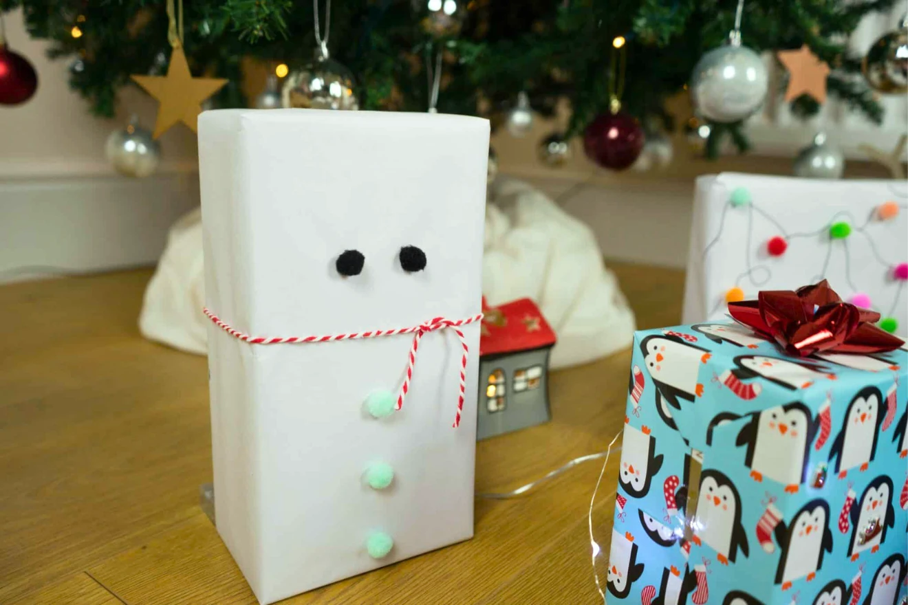 Wrapped gifts under a decorated Christmas tree, including one designed to look like a snowman with buttons and a red and white twine scarf.
