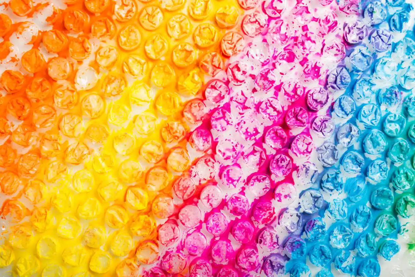 Vibrant rainbow-colored bubble wrap with hues of yellow, orange, pink, purple, and blue in diagonal sections.