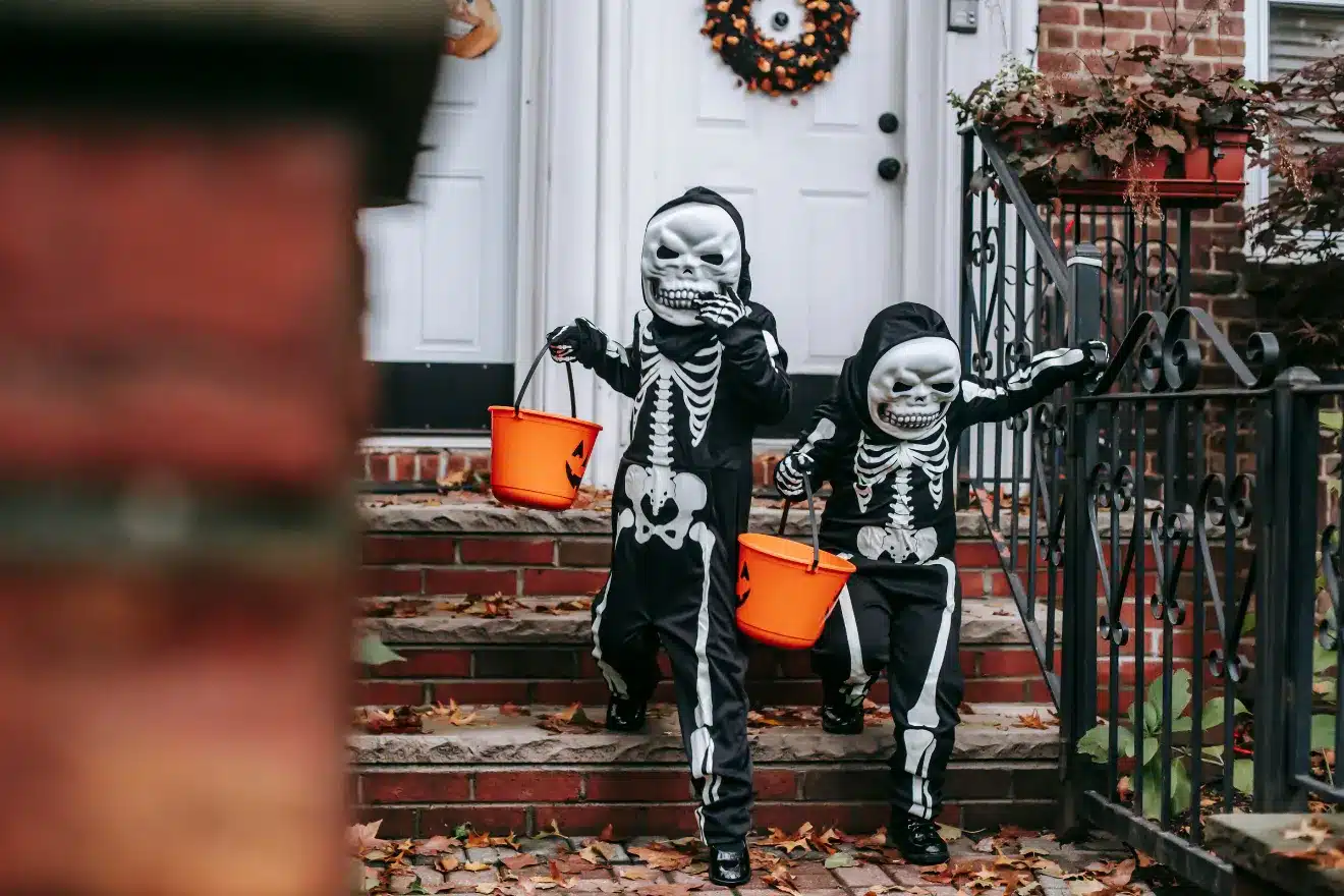 Kids dressed in skeleton costumes walking down the stairs holding Halloween buckets
