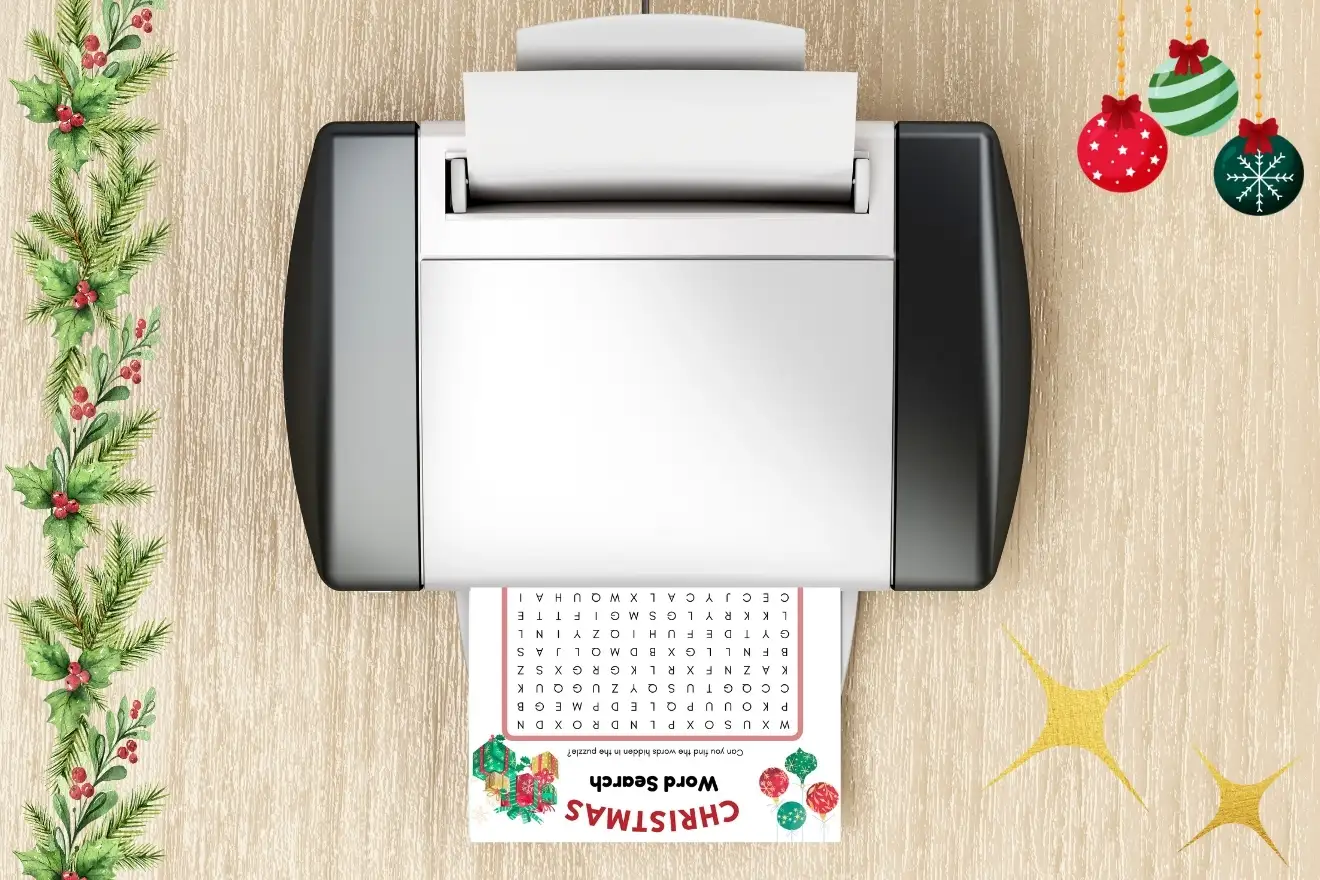 A printer on a wooden surface prints a Christmas-themed word search. Festive decorations and a pine branch are placed nearby.