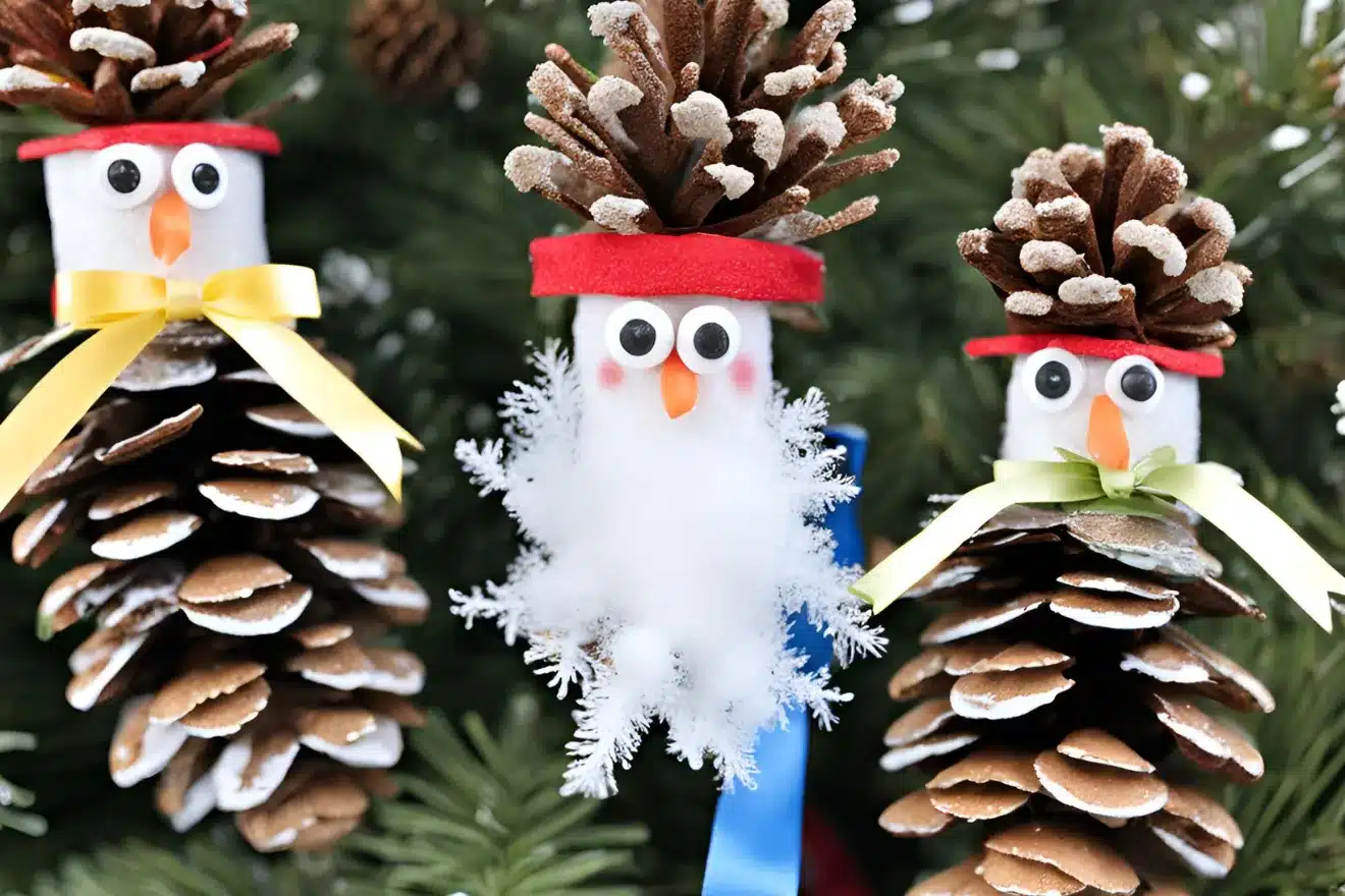 Pine cone crafts decorated as snowmen with googly eyes, felt hats, and ribbons hang on a Christmas tree branch.