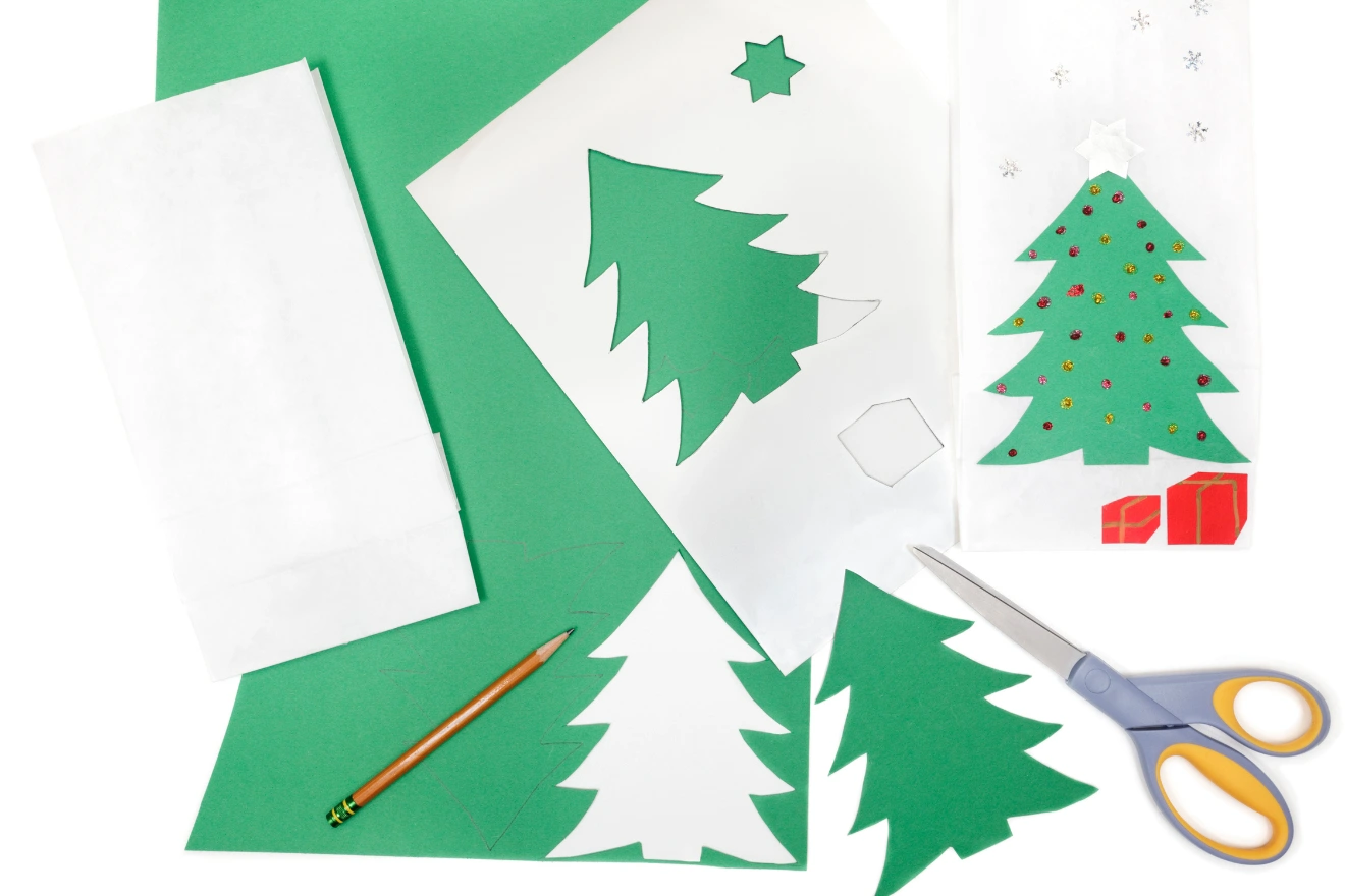 Materials for making Christmas tree crafts, including green and white paper, cut-out shapes, a pencil, scissors, and decorative stickers.
