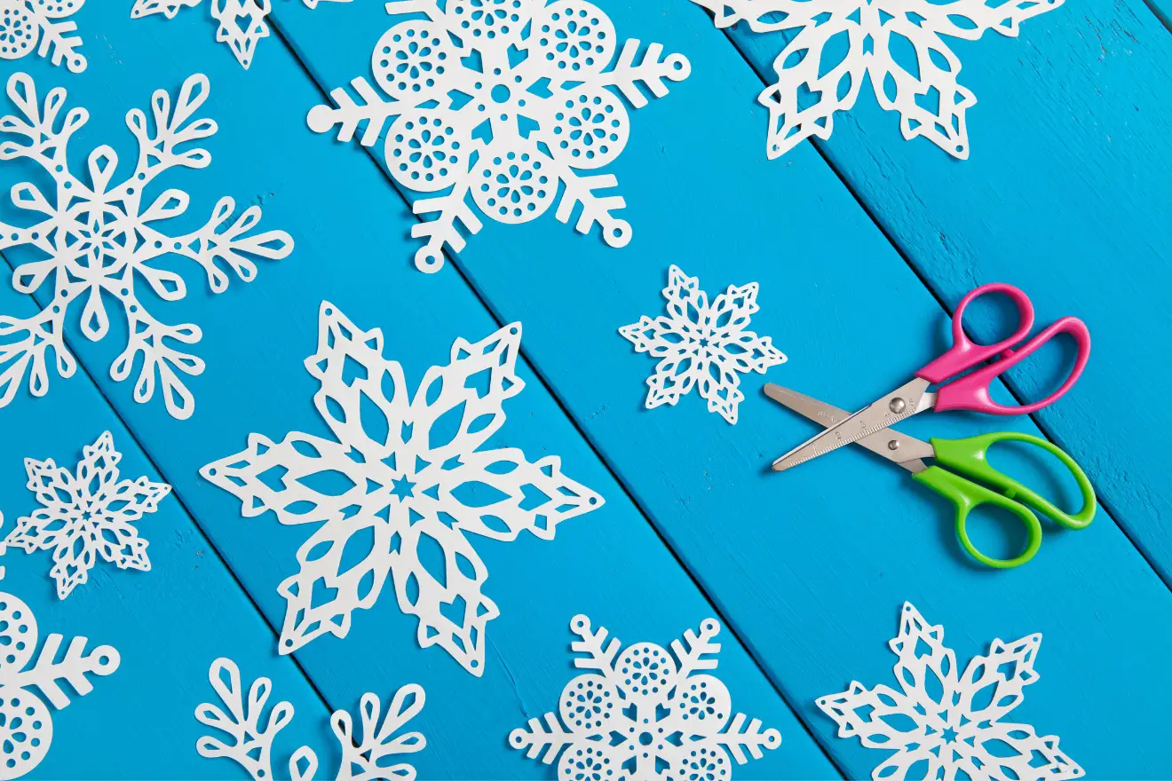 Intricate paper snowflakes on a bright blue surface with pink and green scissors beside them.