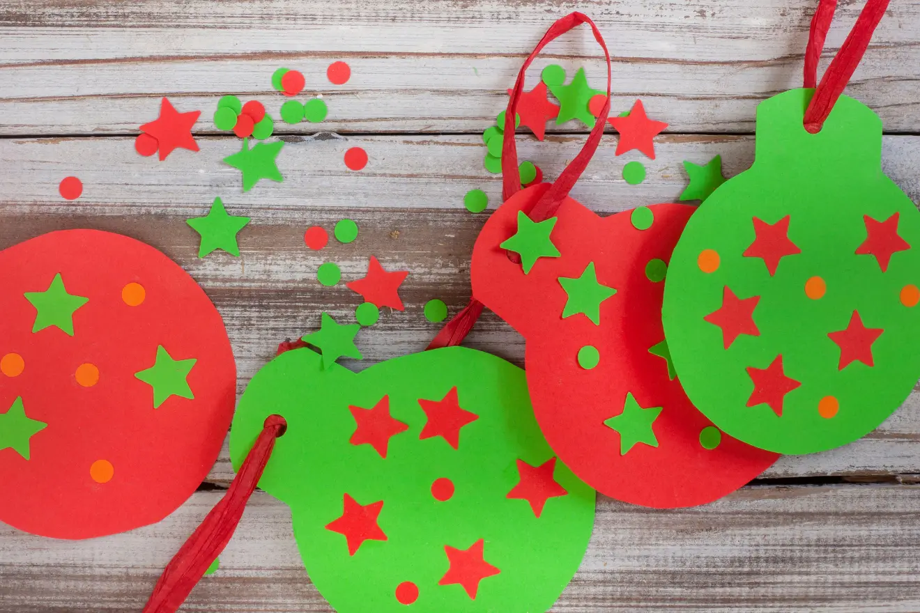 Colorful red and green paper ornaments with star and circle cutouts are scattered on a wooden surface.