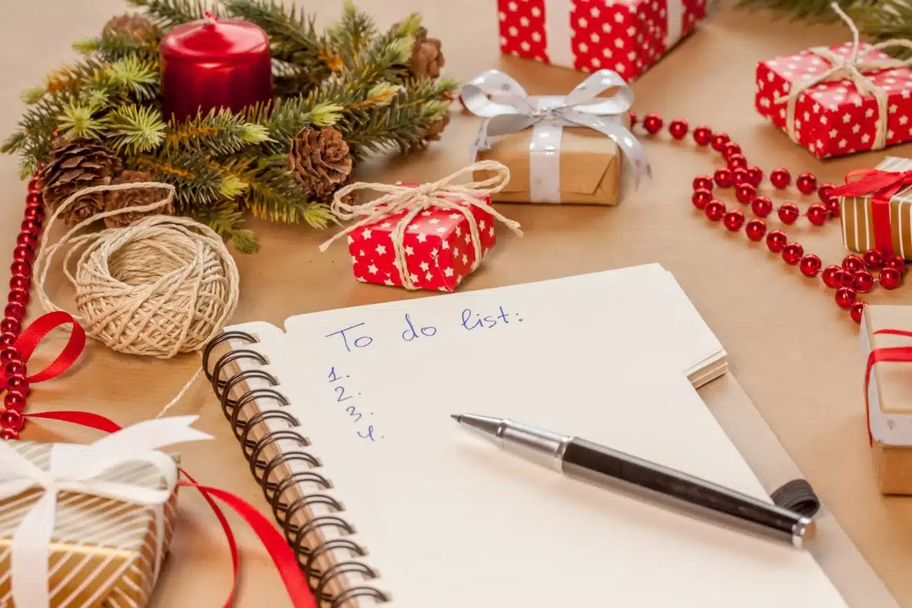 Notebook with "To do list" beside a pen, surrounded by wrapped gifts, a candle, red beads, and pine branch decorations.