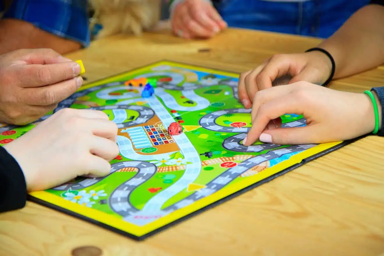 Hands of people playing a colorful board game with game pieces on a wooden table.
