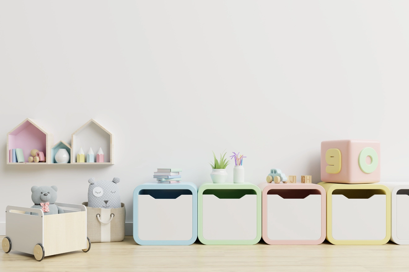 Children's playroom with pastel storage cubes, a toy-filled basket, a teddy bear in a cart, and wall shelves holding small decorations against a white wall.