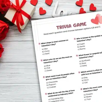 The "Love IQ: Valentine's Day Trivia Game for Kids" sheet sits elegantly on the table, adorned with vibrant red roses, a charming gift box, and delicate heart decorations.
