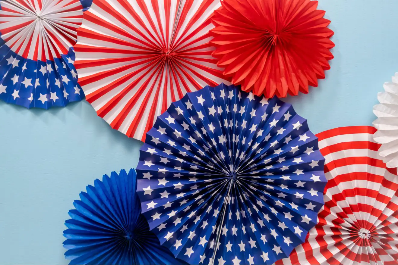 Paper fan decorations in red, white, and blue patterns, including stars and stripes, are arranged against a light blue background.