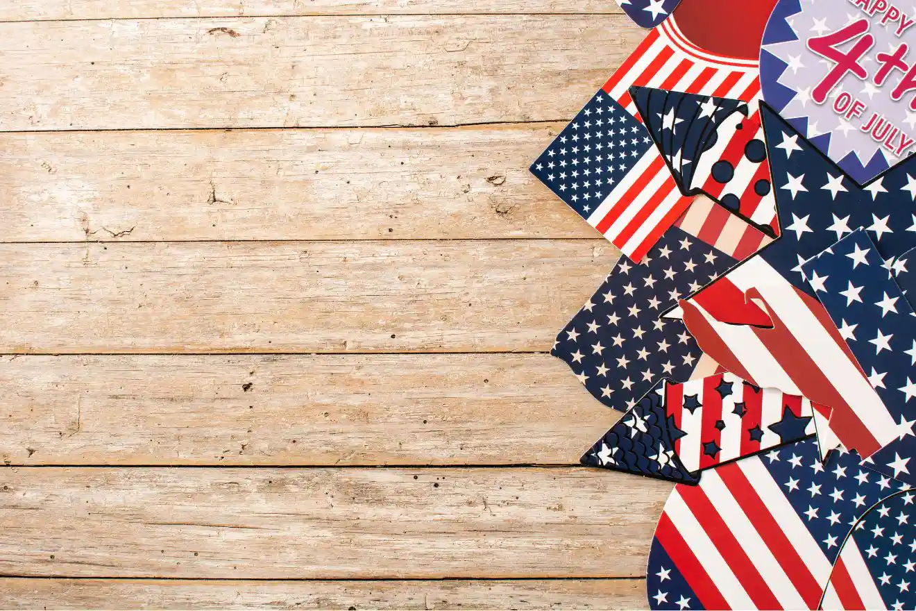 Assorted USA flag-themed party props and signs for the 4th of July arranged on the right side of a wooden surface, with empty space on the left.