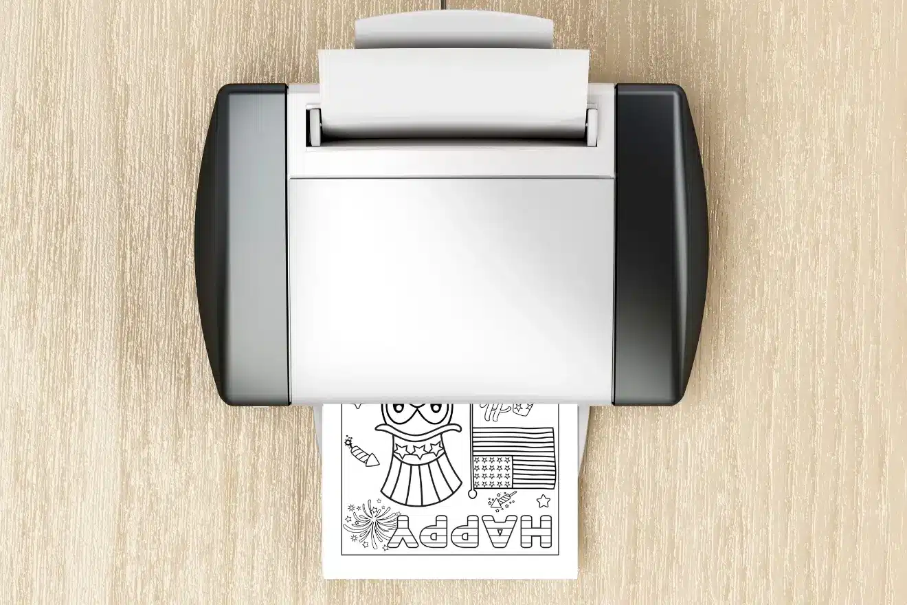 A printer on a wooden surface prints a coloring page with the word "HAPPY" and various outlined drawings and patterns.