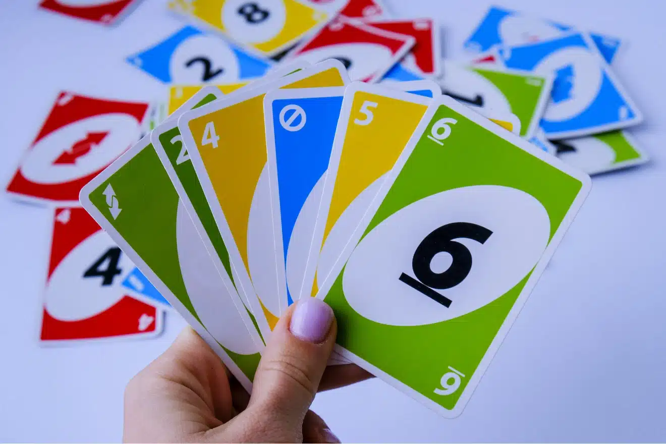 A hand holding six UNO cards—green reverse, yellow 2, yellow 4, blue skip, yellow 5, and green 6—with more UNO cards scattered in the background.