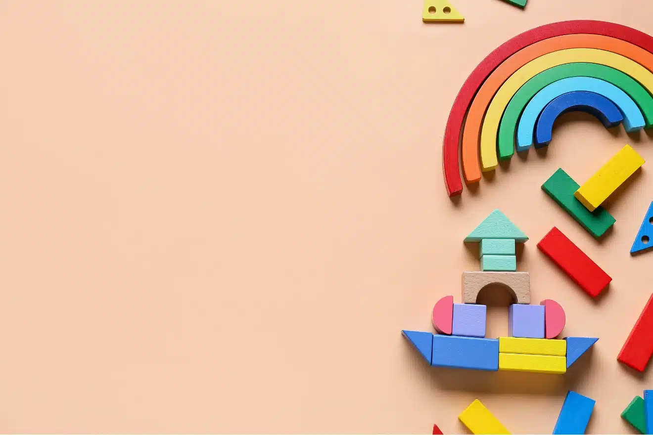 Colorful wooden toy blocks arranged on a beige surface, forming a partial rainbow and various geometric shapes on the right side of the image.