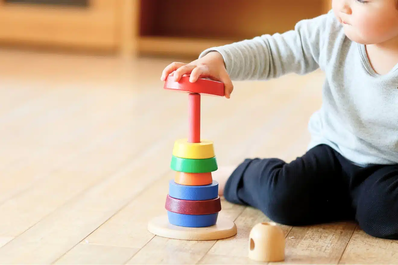 A toddler happily playing with a colorful wooden toy on the floor, focused and engaged in imaginative play.