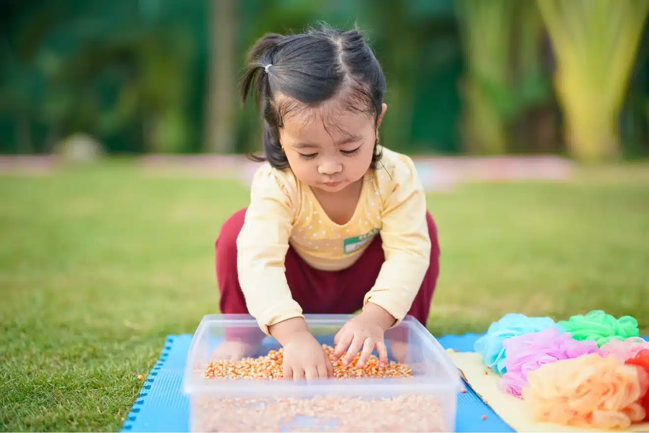 A young girl happily playing with a colorful plastic container filled with food.
