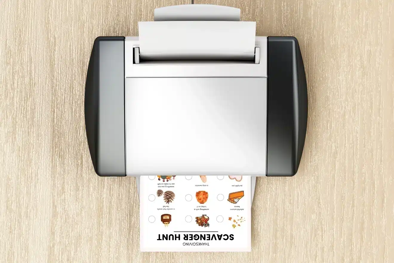 A printer on a wooden surface prints a scavenger hunt sheet with illustrated objects and text.