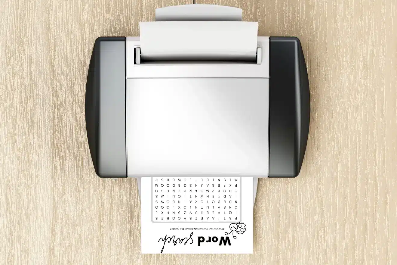 A top-down view of a printer on a wooden surface printing a page with a word search puzzle titled "Word Search.
