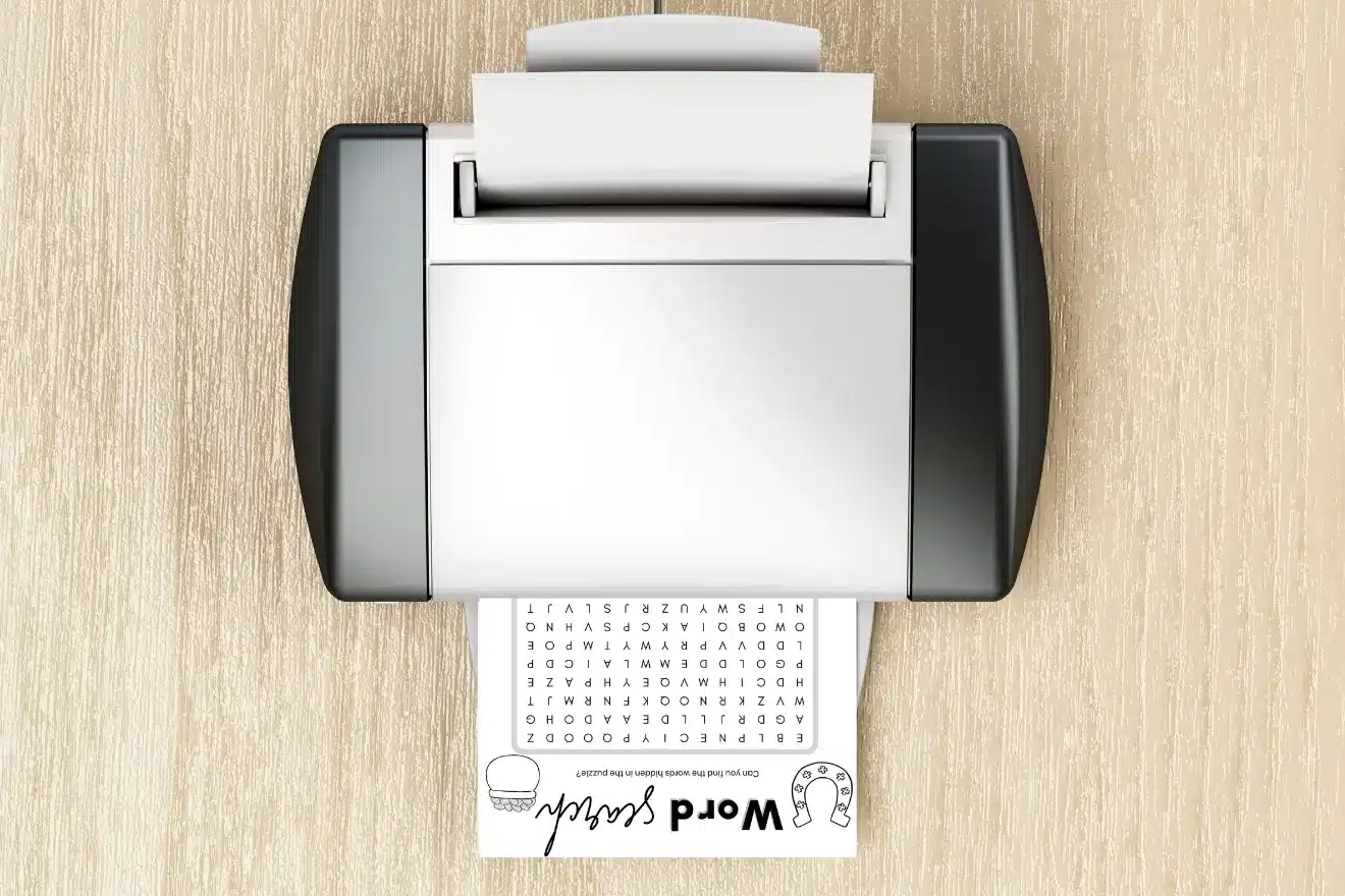 A printer on a wooden desk prints a word search puzzle with images of an ice cream cone and a baseball glove at the bottom.