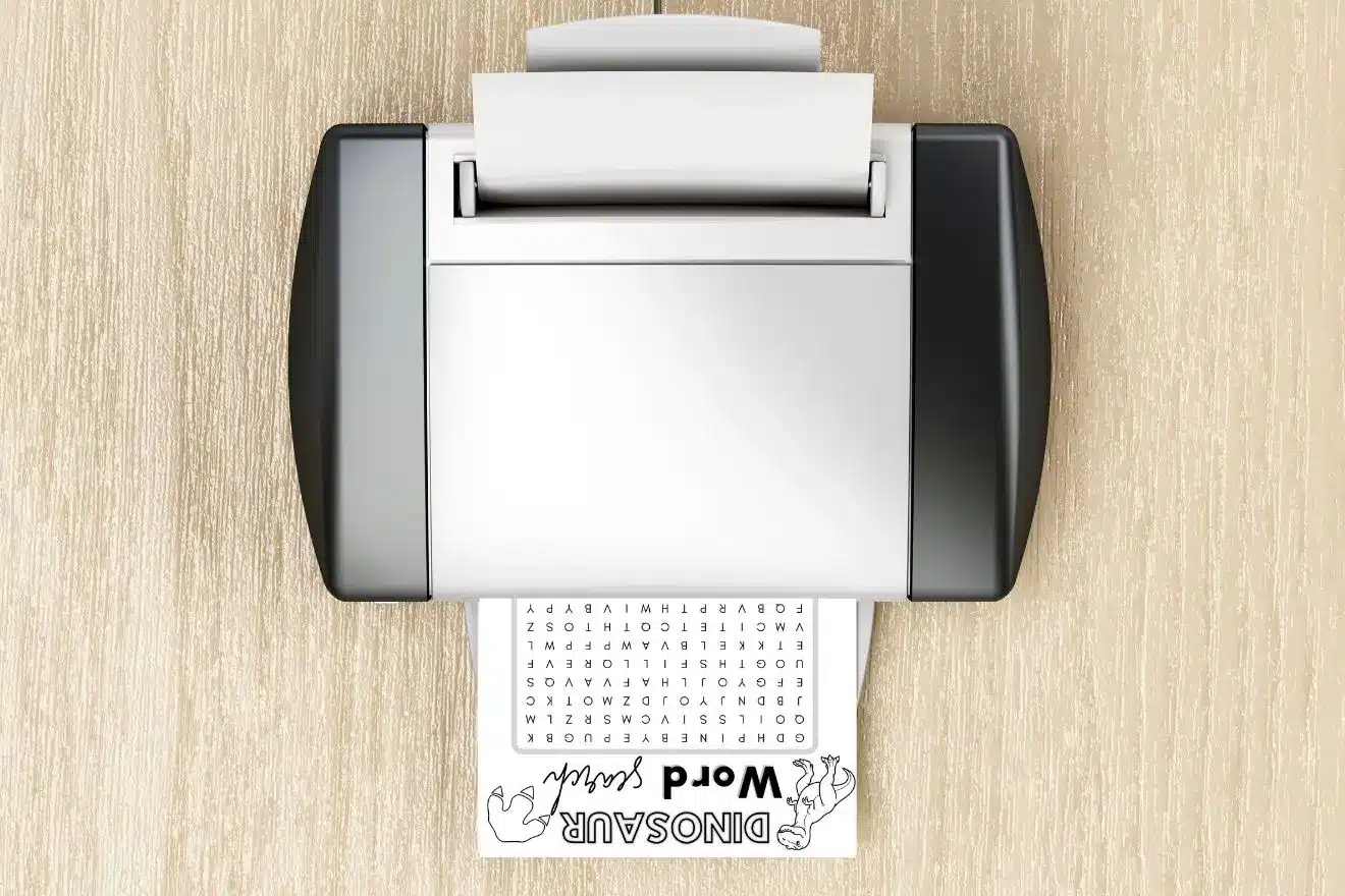 A printer on a wooden surface prints a dinosaur-themed word search puzzle.